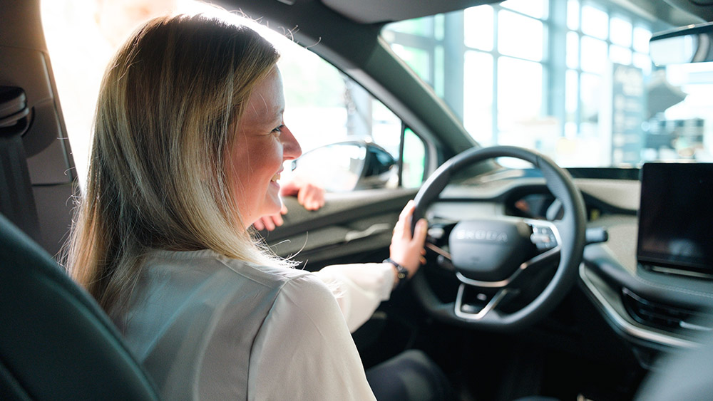 Junge Frau sitzt im Auto und testet das Fahrzeugcockpit – Symbol für Ausbildungs- und Praktikumsmöglichkeiten.
