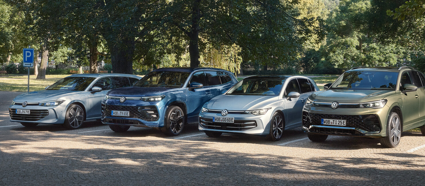 Mehrere Volkswagen Modelle, darunter Passat, Tayron, Golf und Tiguan, stehen nebeneinander auf einem Parkplatz im Grünen