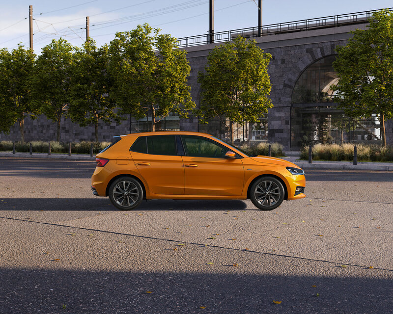 Škoda Fabia in Kupferorange steht seitlich auf einer Straße vor Bäumen und einer Steinbrücke bei Tageslicht.