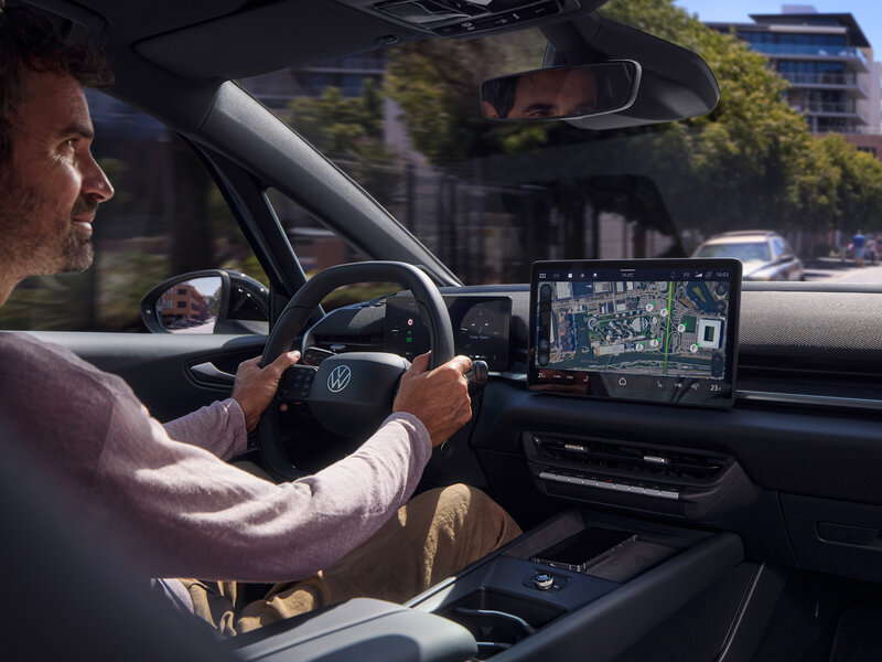 Cockpit des Volkswagen ID.3 Neo mit Fahrer am Lenkrad und Blick auf zentrales Infotainment-Display während der Fahrt durch städtische Umgebung