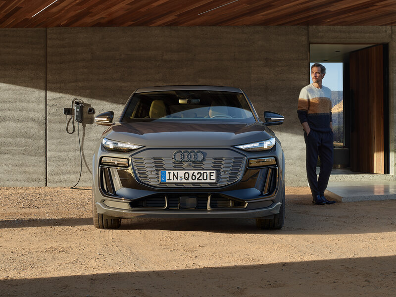 Audi Q6 Sportback e-tron lädt an Wallbox vor modernem Haus mit klarer Front und markanter Lichtsignatur