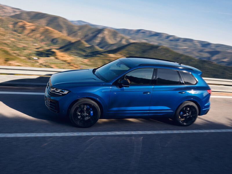 Ein blauer Volkswagen Touareg R eHybrid fährt auf einer kurvigen Bergstraße vor weiter Landschaft.