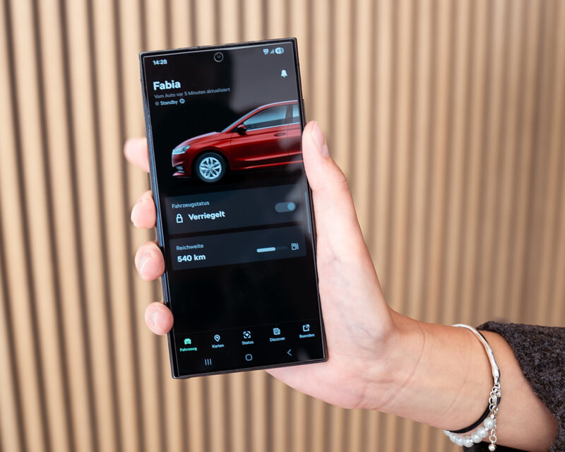 Smartphone mit geöffneter MyŠkoda App, die den Fahrzeugstatus eines roten Škoda Fabia anzeigt