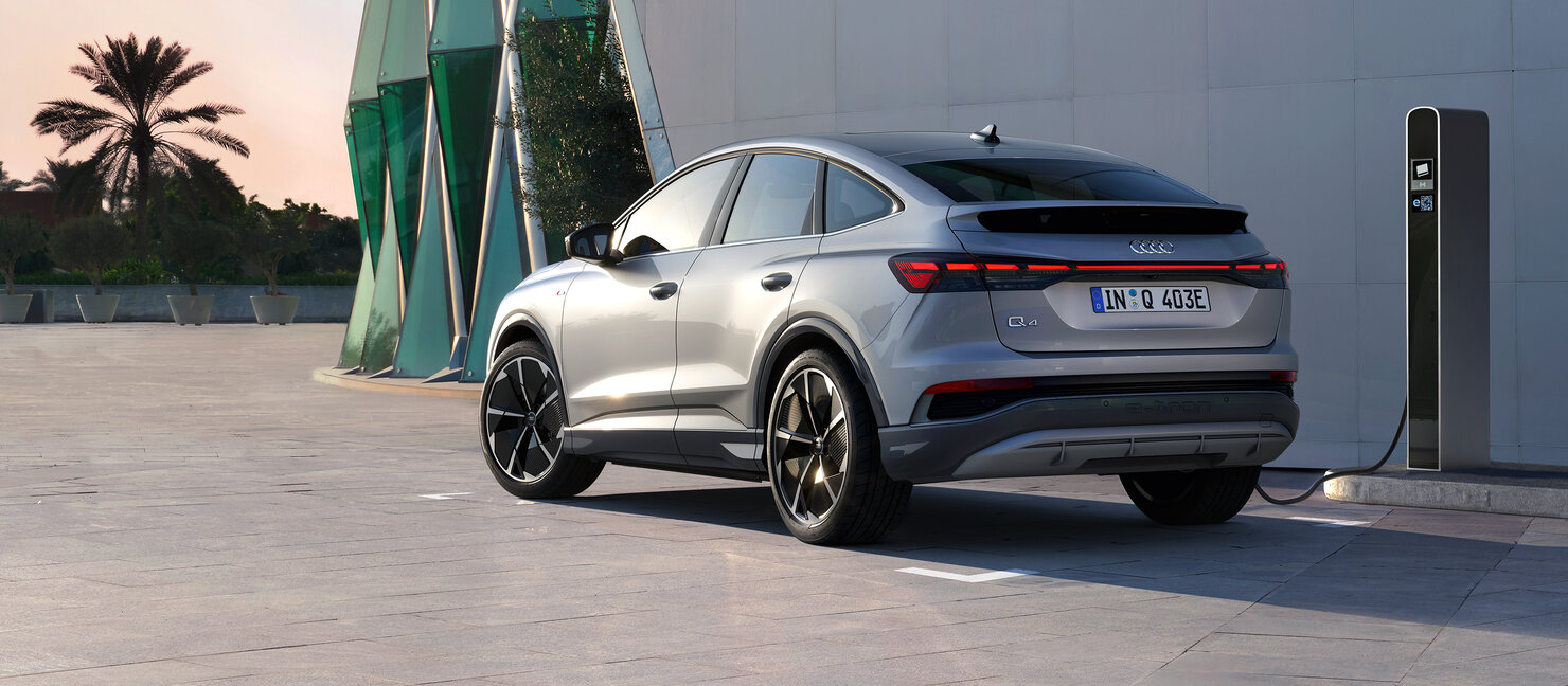 Audi Q4 Sportback e-tron schräg von hinten an einer Ladesäule, betont durch LED-Heckleuchten und aerodynamisches Design