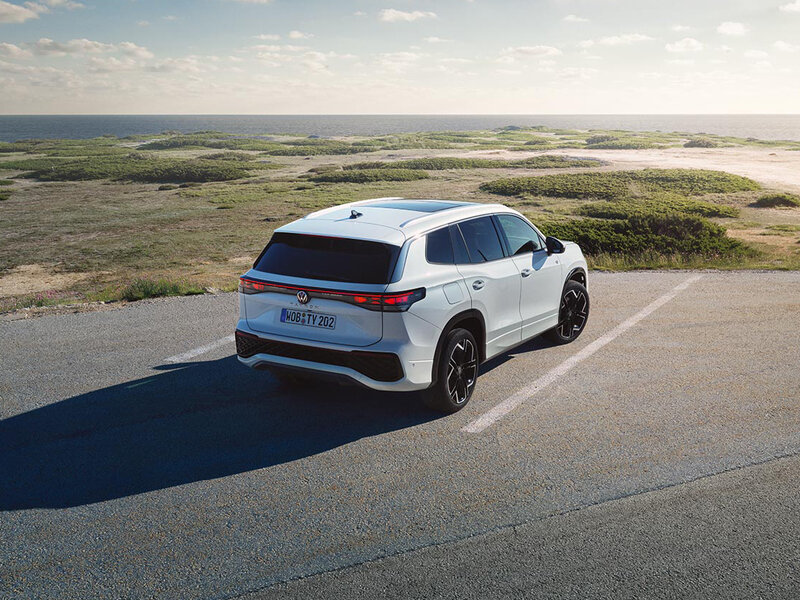 Ein weißer Volkswagen Tayron steht auf einer Straße mit Blick auf eine weitläufige Küstenlandschaft.