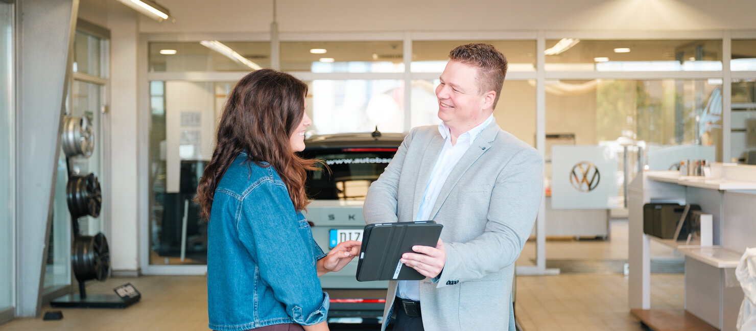 Zwei Personen stehen in der Volkswagen Werkstatt von Auto Bach in Limburg vor einem Fahrzeug und besprechen Details mit einem Tablet
