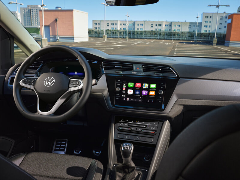 Fahrerperspektive auf das Cockpit eines Volkswagen Touran mit Digitaldisplay, Touchscreen-Infotainmentsystem und manuellem Schaltgetriebe.