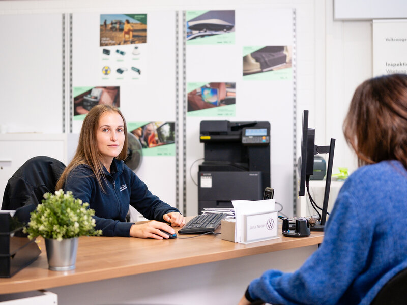 Mitarbeiterin im Auto Bach Servicebereich führt ein Beratungsgespräch mit Kundin am Schreibtisch eines Volkswagen Autohauses