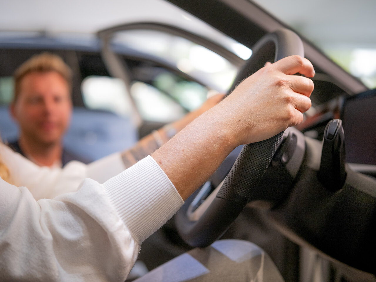 Person hält das Lenkrad eines Fahrzeugs im Auto Bach Showroom, während ein Mitarbeiter neben dem Auto hockt