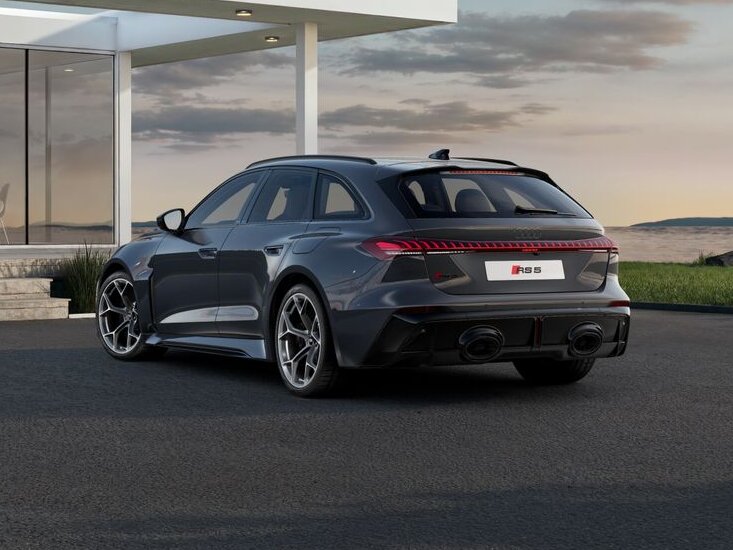 Audi RS5 Avant von hinten schräg geparkt vor moderner Architektur mit Glasfassade auf asphaltierter Fläche bei Abendlicht