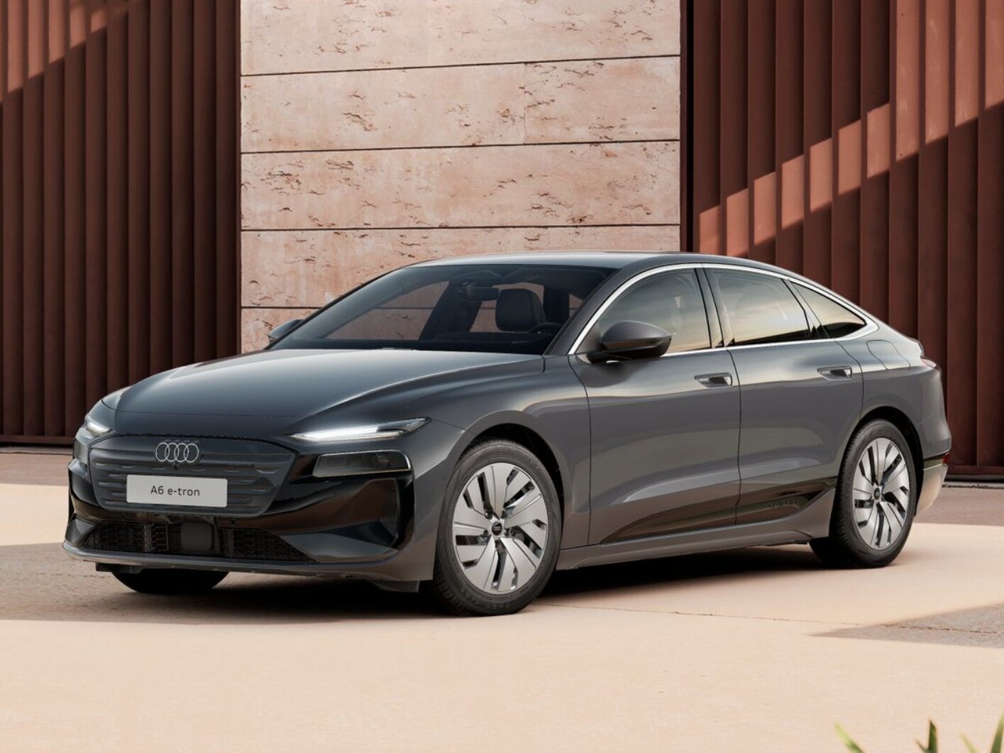 Dunkelgrauer Audi A6 e-tron steht vor moderner Architektur mit strukturierter Fassade in ruhiger Umgebung