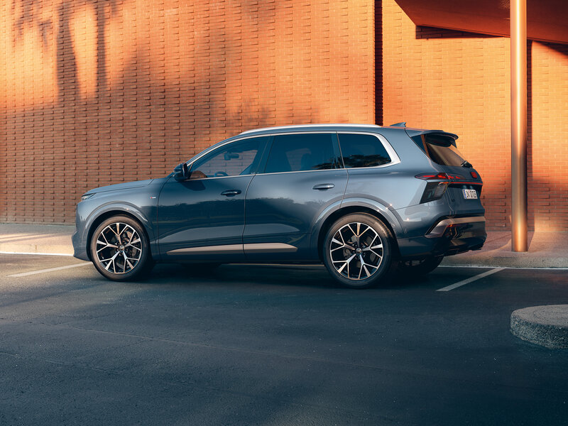 Audi Q7 in Seitenansicht auf einer Zufahrt vor moderner Architektur mit warmem Sonnenlicht und markanter Fahrzeugsilhouette