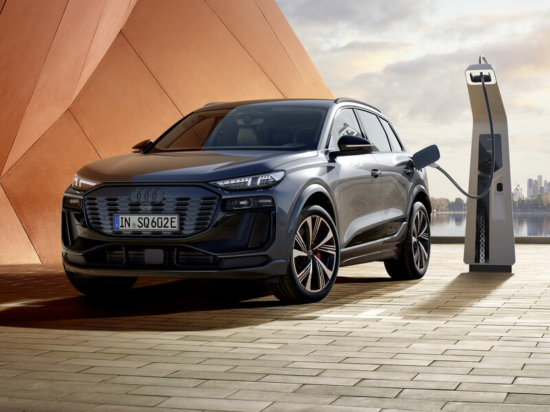 Audi SQ6 e-tron lädt an Ladesäule vor moderner Architektur, frontal-seitliche Ansicht des SUVs