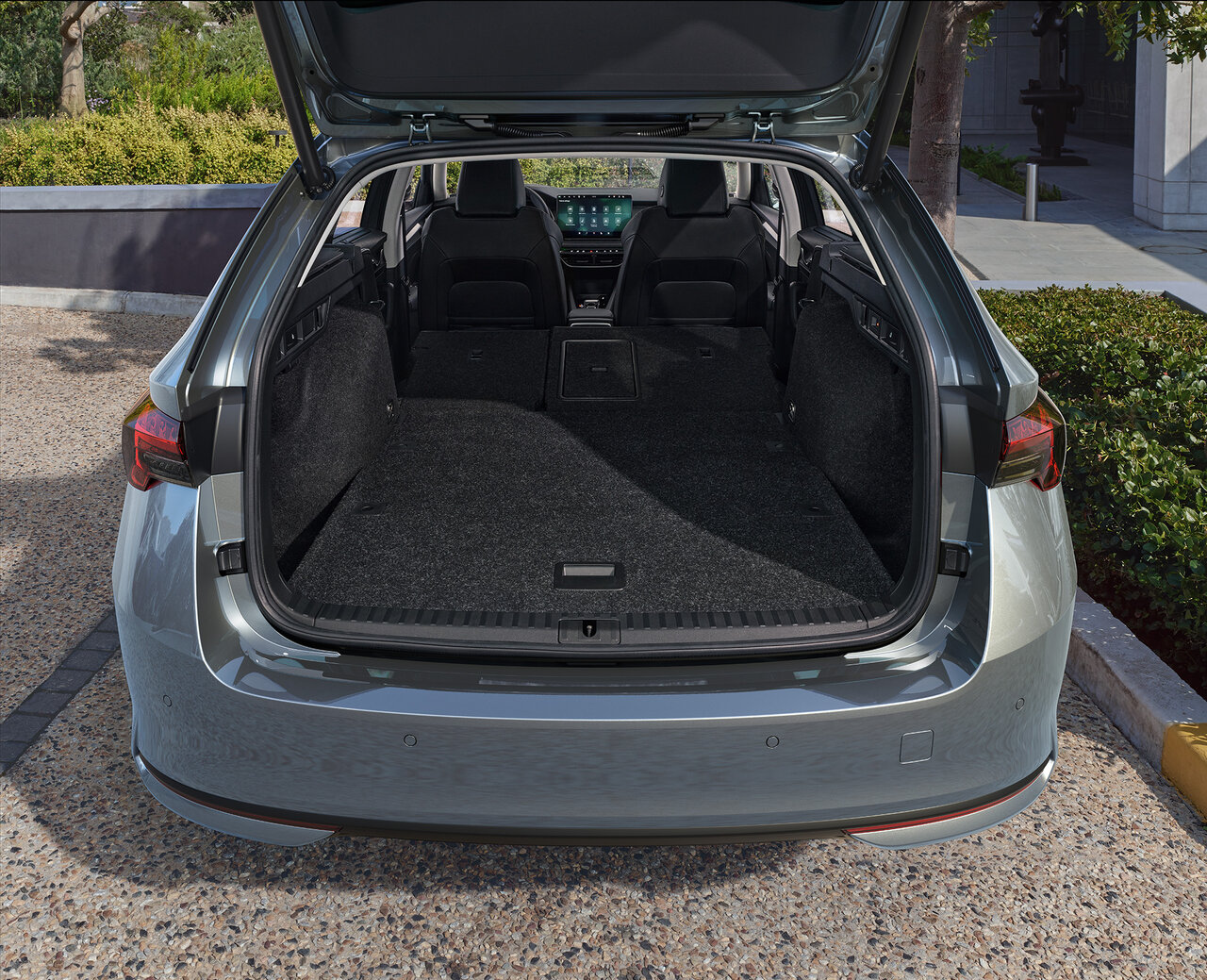 Offener Kofferraum eines grauen Škoda Octavia Combi mit umgeklappter Rücksitzbank auf einem gepflasterten Parkplatz.