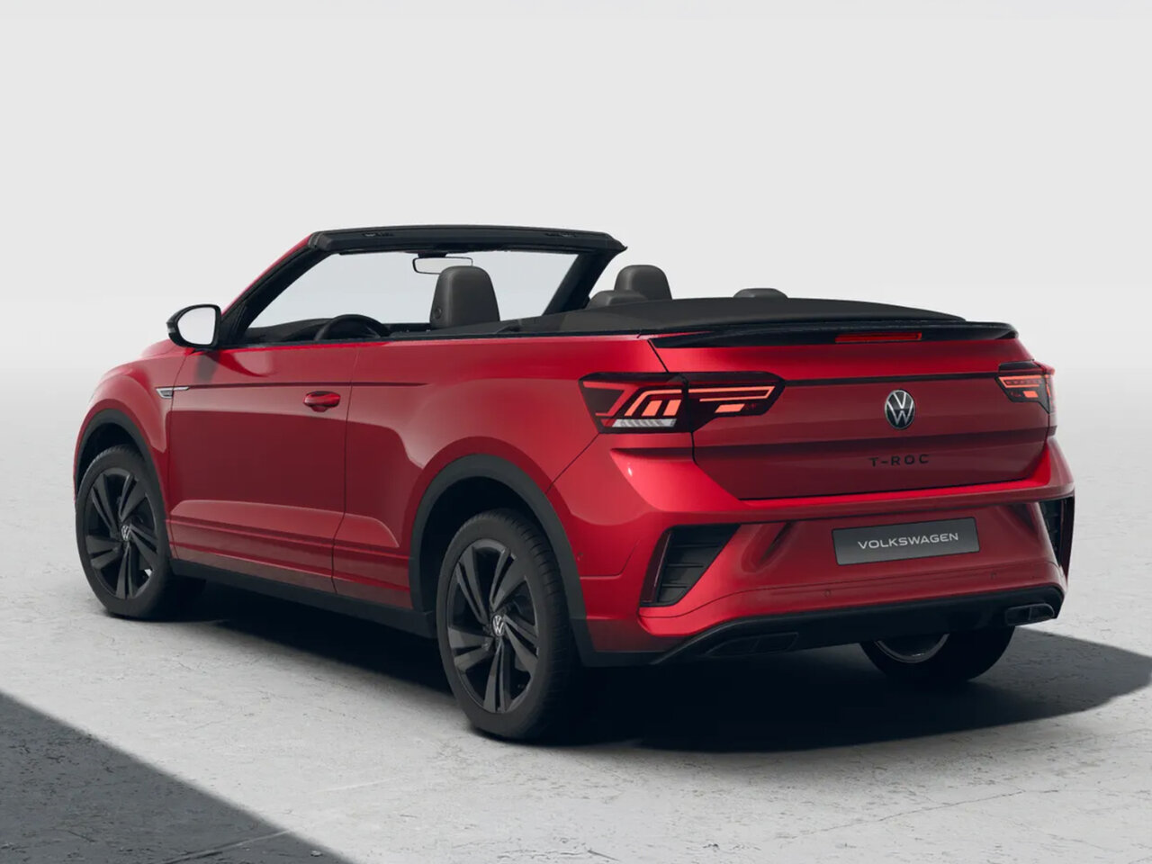 Rotes Volkswagen T-Roc Cabriolet mit geöffnetem Verdeck in schräger Heckansicht und schwarzen Felgen vor neutralem hellem Hintergrund