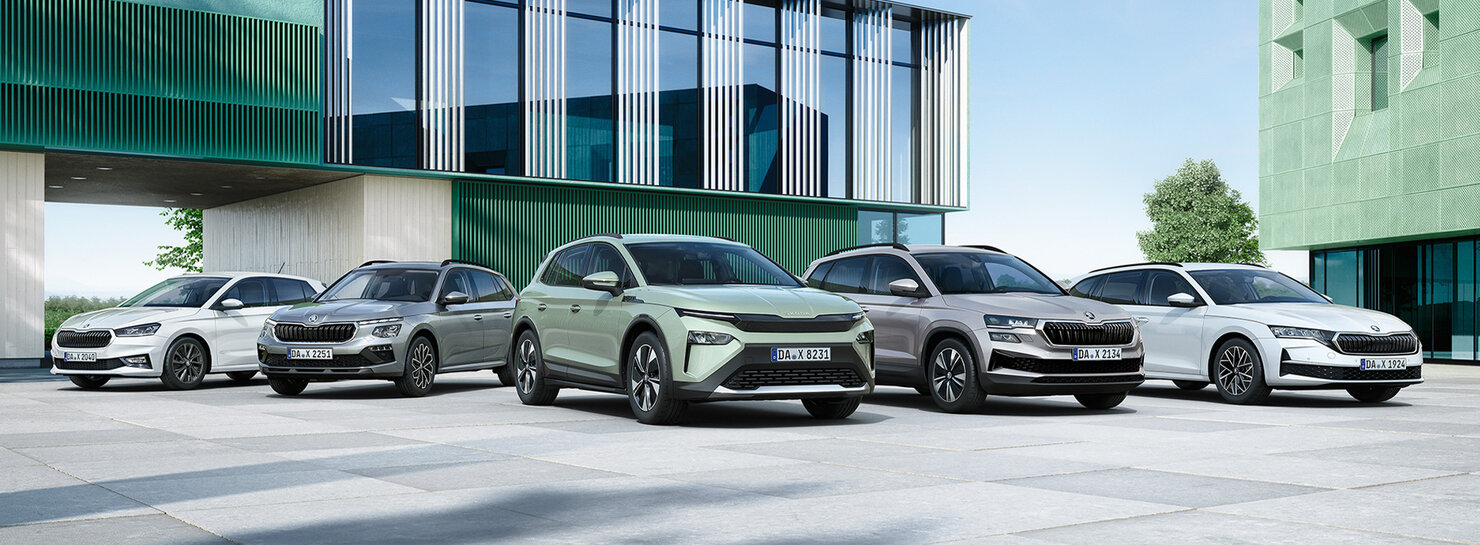 Fünf Škoda Modelle stehen in Reihe vor modernem Autohausgebäude auf großem Vorplatz in Frontansicht