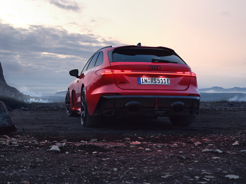 Audi RS 5 Avant in Rot aus Heckperspektive auf Schotterfläche vor Berglandschaft bei Sonnenuntergang