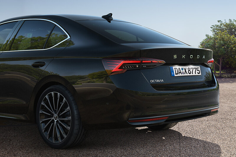 Heckansicht eines schwarzen Škoda Octavia Limousine auf einem Parkplatz mit Bäumen im Hintergrund bei sonnigem Wetter.