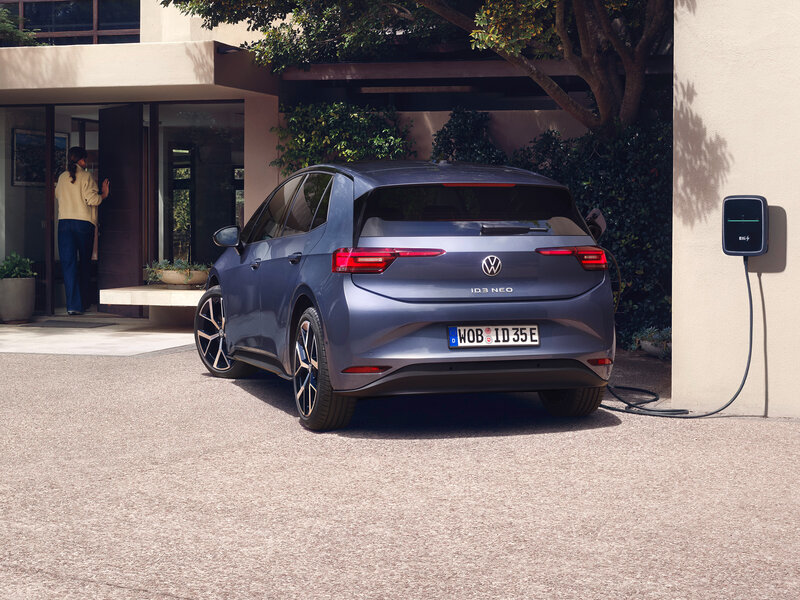 Heckansicht des Volkswagen ID.3 Neo beim Laden an einer Wallbox vor modernem Wohnhaus mit Einfahrt und begrünter Fassade
