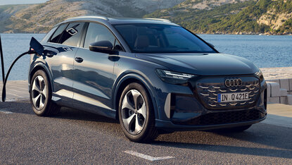 Audi Q4 e-tron steht seitlich an Ladesäule auf Parkplatz an einer Küstenstraße mit Bergen und Wasser im Hintergrund
