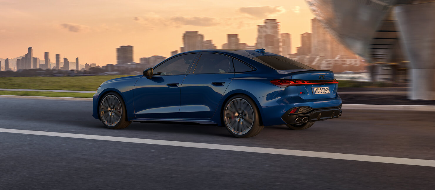 Audi S5 Limousine in Bewegung vor städtischer Kulisse bei Abendlicht, sportliches Design und fließende Linien sichtbar
