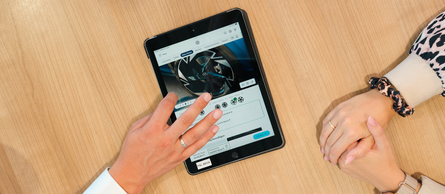 Beratungsgespräch im Auto Bach Autohaus, bei dem auf einem Tablet Volkswagen Felgenkonfiguration angezeigt wird