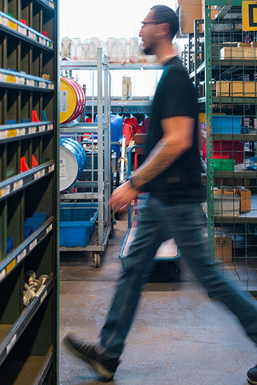 Mitarbeiter bewegt sich durch ein Lager mit Regalen und organisiert Bauteile für einen reibungslosen Ablauf.