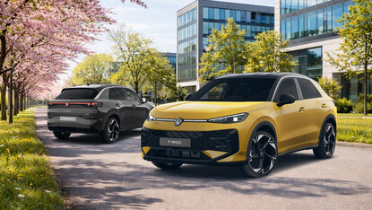 „Zwei Volkswagen T-Roc R-Line fahren auf einer Straße zwischen blühenden Bäumen vor modernen Bürogebäuden