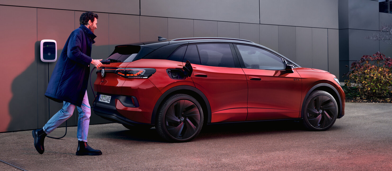 Volkswagen ID.4 GTX in Rot wird an einer Wallbox vor einem modernen Gebäude geladen