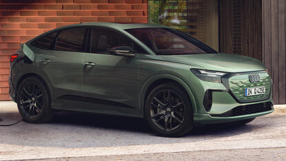 Audi Q4 Sportback e-tron in Grün lädt an Wallbox vor Backsteinfassade aus seitlicher Perspektive auf einer Einfahrt