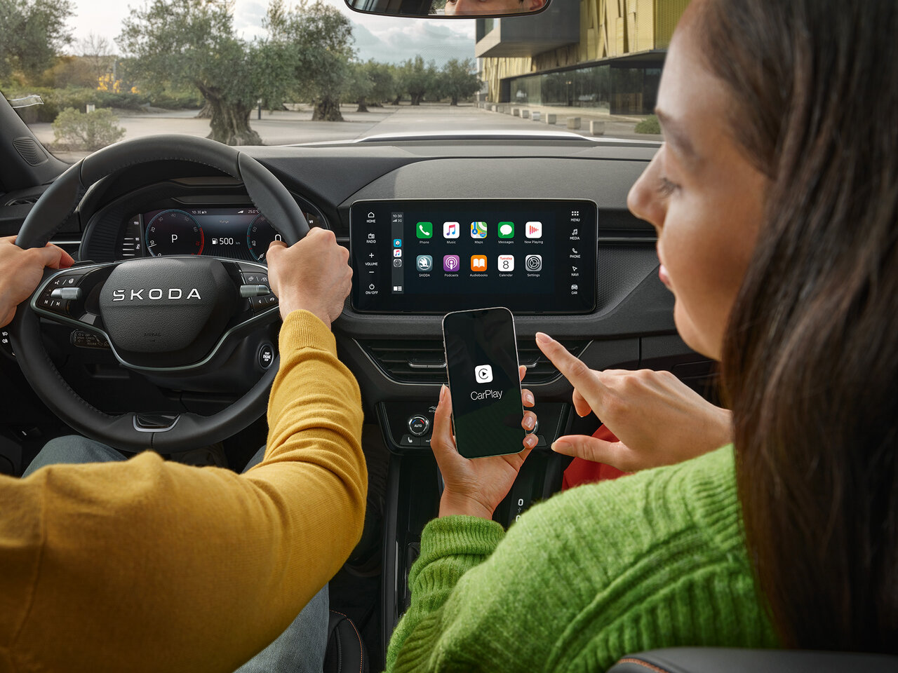 Zwei Personen sitzen im Škoda Kamiq, eine hält ein Smartphone mit verbundenem Infotainmentsystem auf dem zentralen Display.