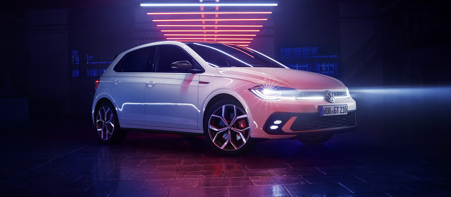 Volkswagen Polo GTI in Weiß steht in einer dunklen Halle mit neonfarbener Beleuchtung und eingeschalteten Frontscheinwerfern.