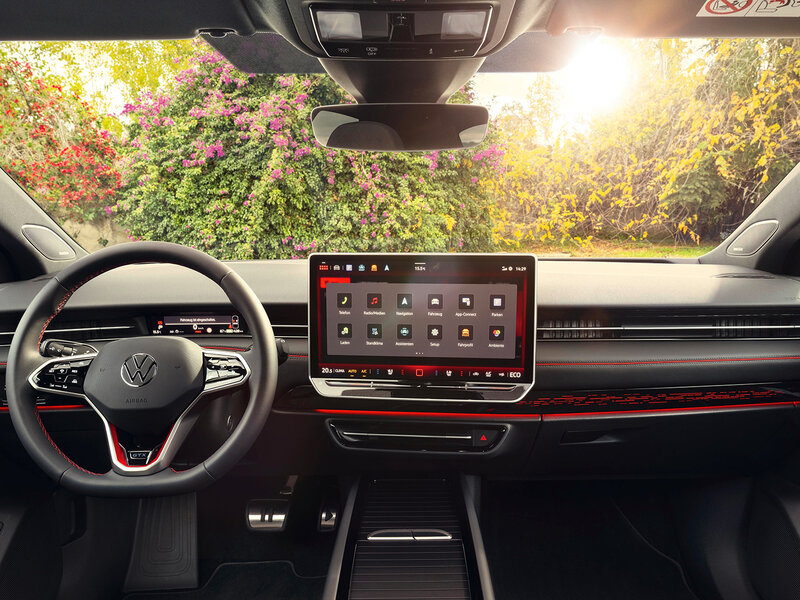 Innenraum des VW ID.7 GTX mit großem Touchdisplay, Multifunktionslenkrad und roter Ambientebeleuchtung.