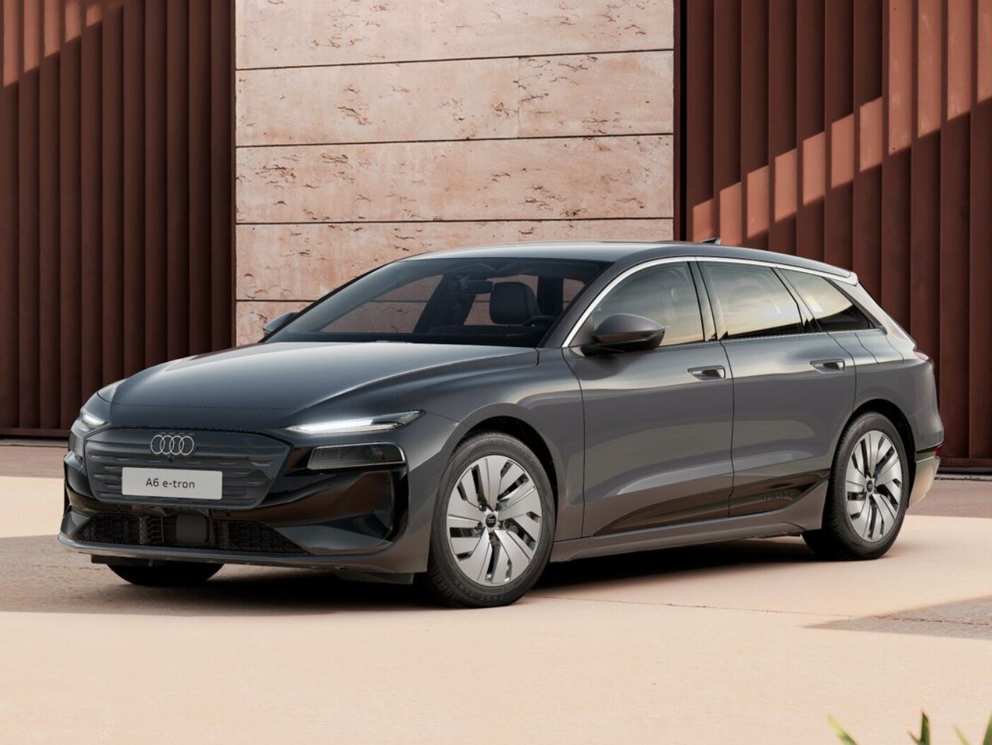 Dunkelgrauer Audi A6 Avant e-tron in Frontansicht steht vor moderner Architektur mit strukturierter Fassade und hellem Außenbereich