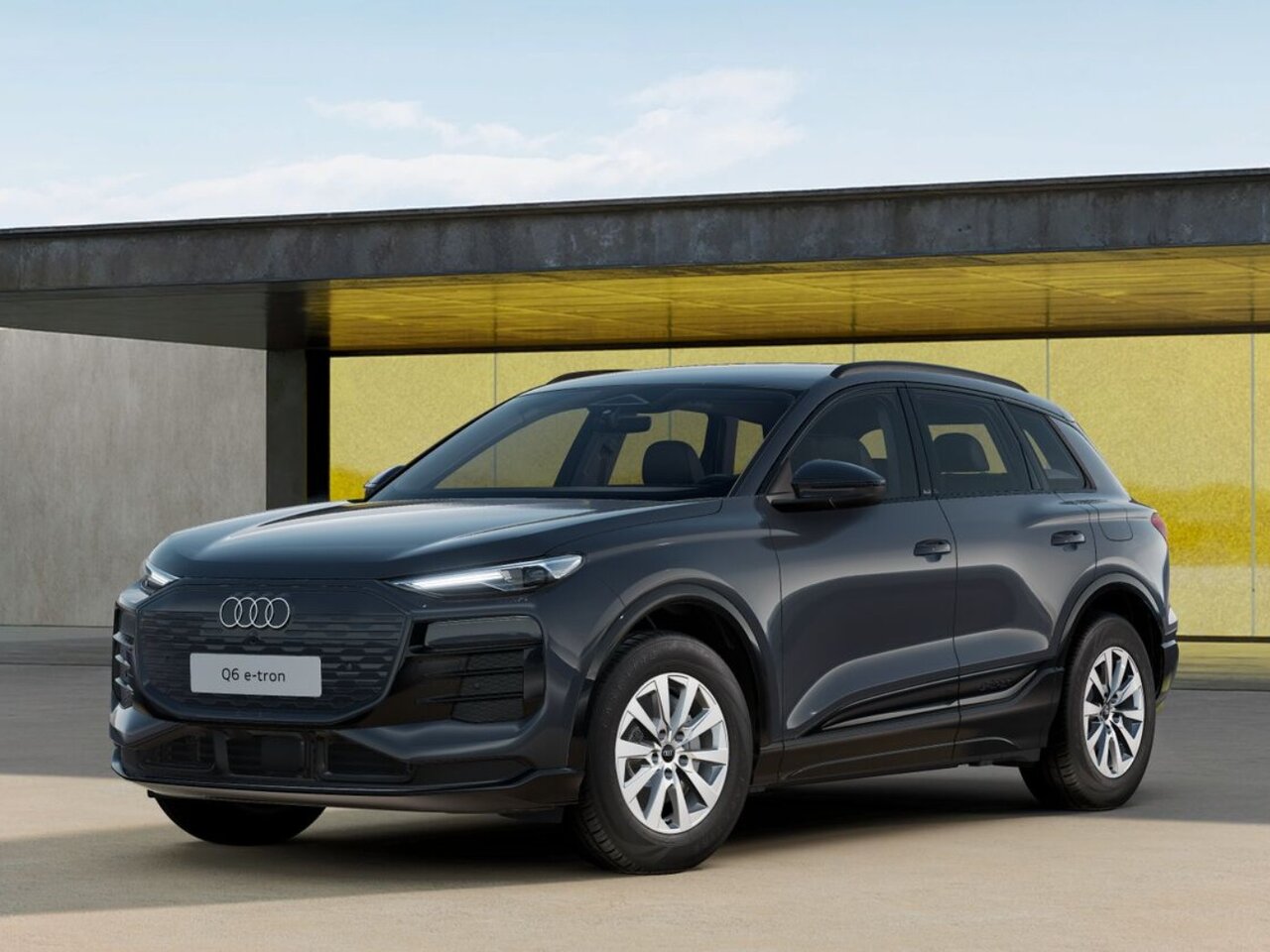 Dunkelgrauer Audi Q6 e-tron steht vor moderner Architektur mit Glasfassade und flachem Vordach bei Tageslicht