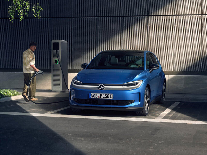 Volkswagen ID. Polo in Blau in Frontansicht steht auf Parkplatz während eine Person das Fahrzeug an einer Ladesäule lädt