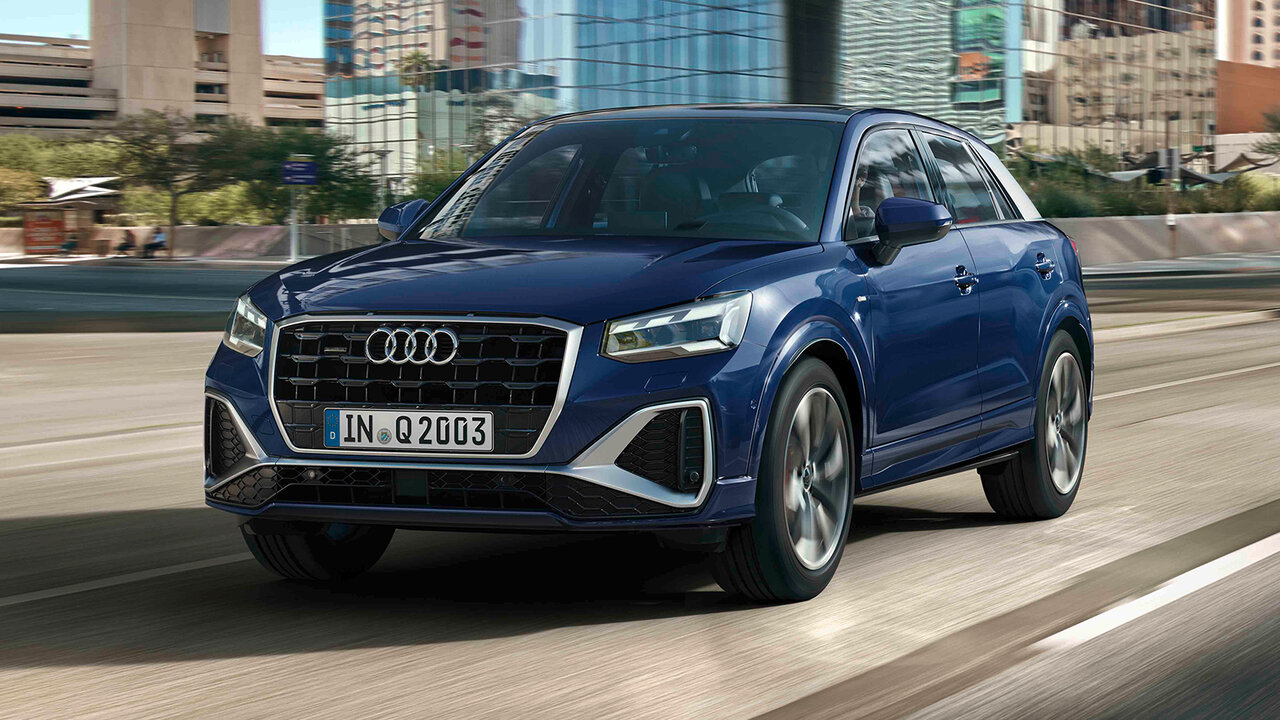 Audi Q2 in Blau fährt auf mehrspuriger Straße durch urbane Umgebung mit moderner Architektur im Hintergrund