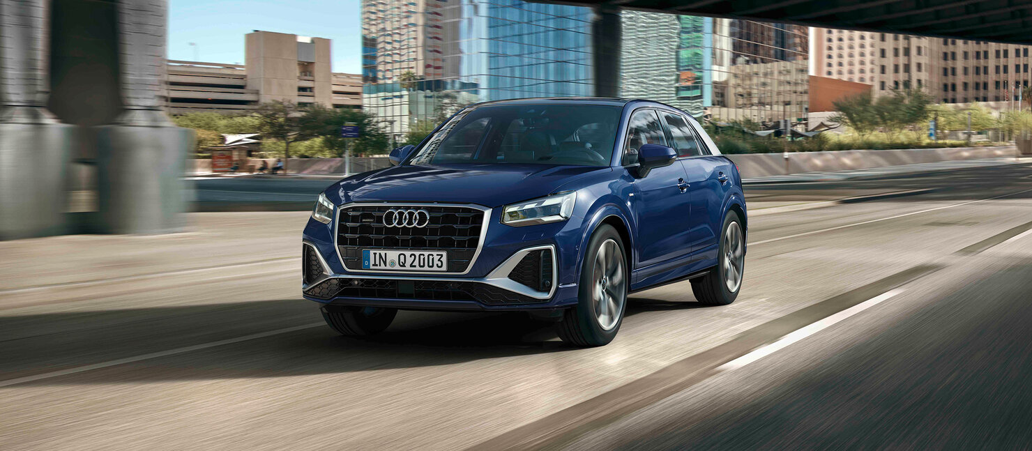Audi Q2 in dynamischer Fahraufnahme auf Stadtstraße, Frontansicht mit markantem Singleframe-Grill und LED-Lichtsignatur