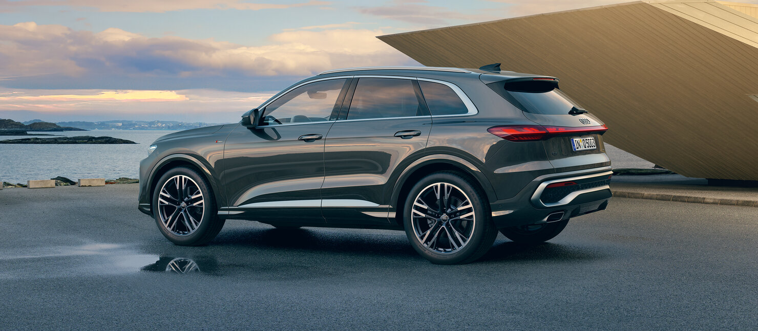 Audi Q5 steht seitlich an der Küste, sportlich-elegantes SUV-Design vor Meer, Himmel und moderner Gebäudeform