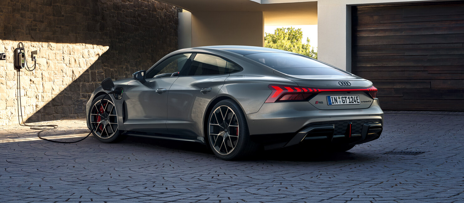 Audi RS e-tron GT schräg von hinten vor moderner Architektur, betontes Heckdesign mit Leuchtenband und sportlicher Elektro-Performance