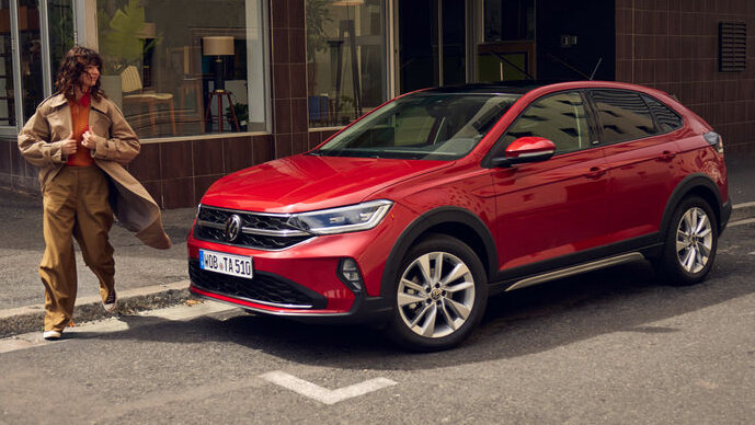 Roter Volkswagen Taigo steht am Straßenrand vor einem Gebäude, eine Person geht auf dem Gehweg daneben entlang