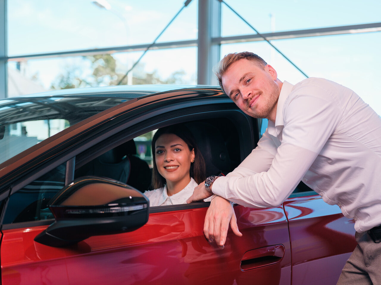 Eine Frau sitzt in einem roten Auto, während ein Auto Bach Mitarbeiter ihr im Showroom eine Fahrzeugfunktion erklärt
