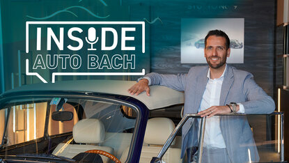 Sebastian Bach steht neben einem VW Käfer Cabrio im Showroom vor dem Schriftzug „Inside Auto Bach“