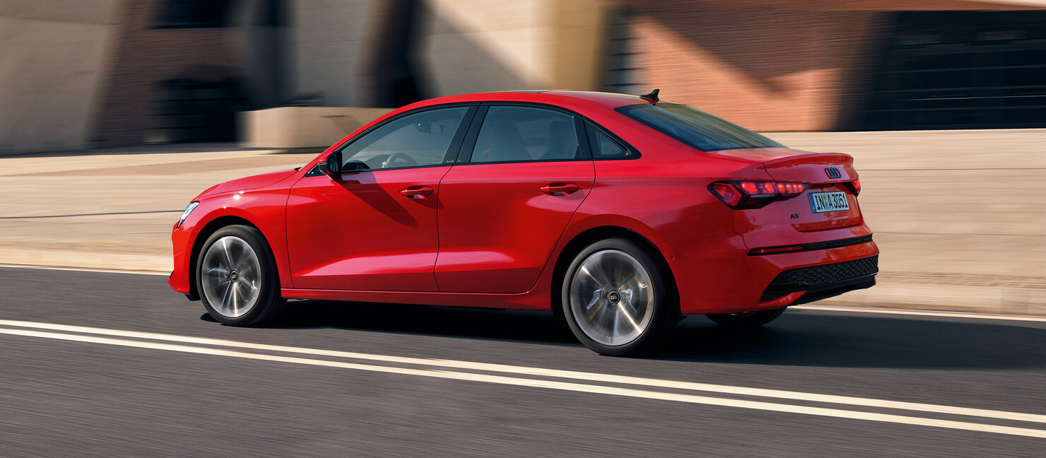 Rote Audi A3 Limousine in seitlicher Heckansicht auf urbaner Straße, klare Linien und coupéhafte Silhouette