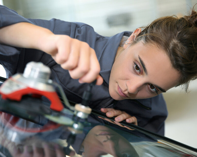 Kfz-Mechanikerin repariert Steinschlag an einer Autoscheibe mit professionellem Werkzeug in der Werkstatt.