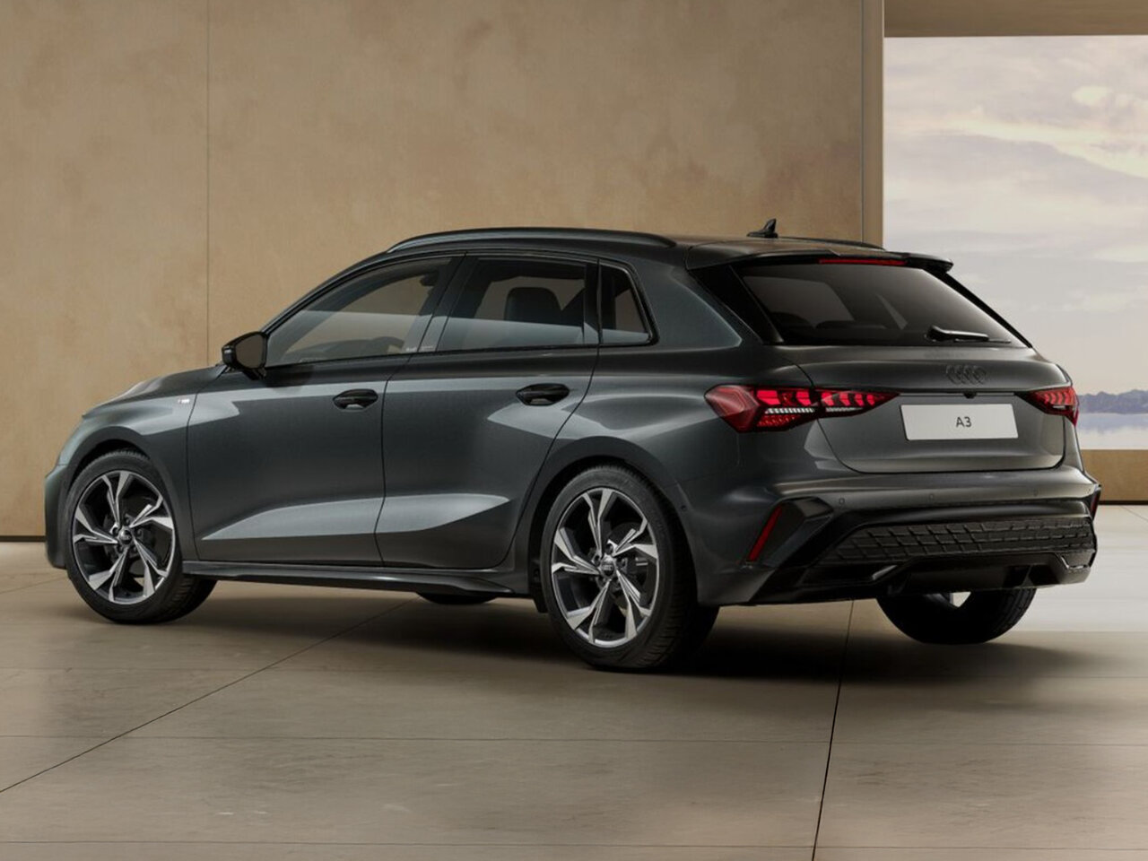 Dunkelgrauer Audi A3 Sportback in Heckansicht steht in modernem Innenraum mit Landschaft im Hintergrund
