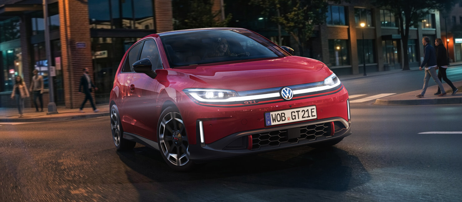 Volkswagen ID. Polo GTI in Rot fährt bei Dämmerung durch eine Innenstadtstraße aus Frontperspektive