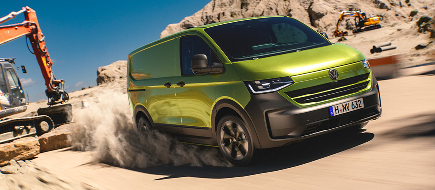 Grüner Volkswagen Transporter fährt über staubige Baustelle, Bagger arbeiten im Hintergrund.