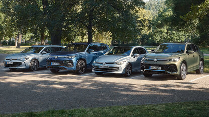 Vier Volkswagen Hybrid-Modelle stehen nebeneinander auf einem Parkplatz im Grünen bei Tageslicht