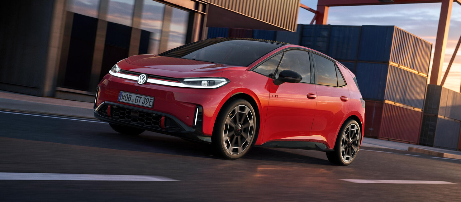Roter Volkswagen ID.3 GTI aus schräger Frontperspektive auf einer Straße vor moderner Industriearchitektur bei tief stehender Sonne